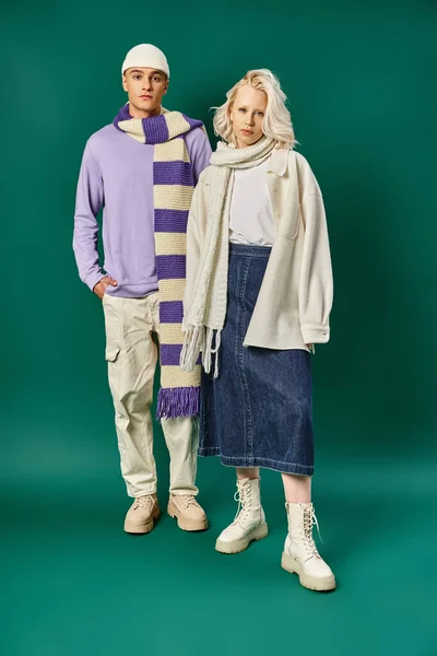 Trendfarben, Mann in entkleidetem Schal und Mütze posiert mit schöner Frau vor türkisfarbenem Hintergrund — Stockfoto