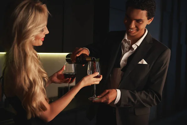 Joyeux multiracial beau couple en tenue de soirée se préparant à boire du vin rouge à la maison — Photo de stock