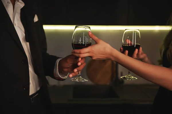 Vista cortada de casal jovem multicultural trocando copos com vinho tinto em casa à noite — Fotografia de Stock