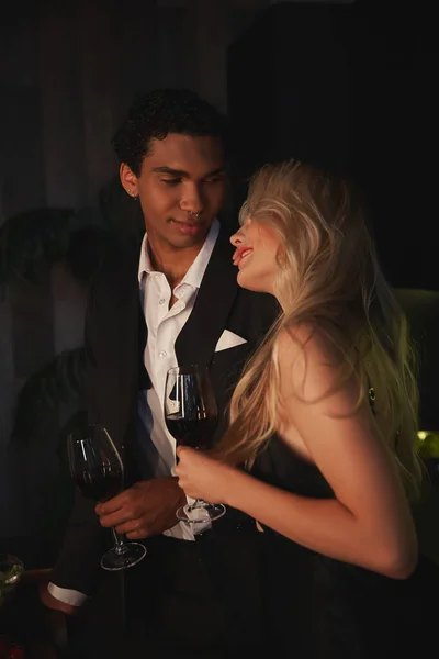 Cheerful young multicultural couple in elegant attires spending time together and drinking red wine — Stock Photo