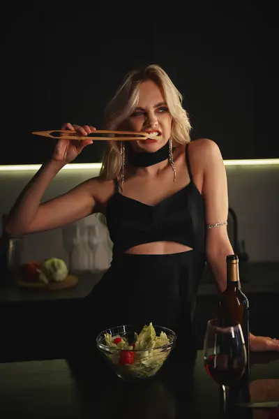 Gut aussehende blonde Frau im schwarzen schicken Kleid isst frischen Salat mit Stäbchen — Stockfoto