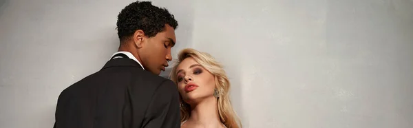 Attraktives, vielseitiges Paar in eleganten Abendkleidern posiert gemeinsam auf grauem Hintergrund, Banner — Stockfoto