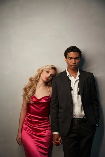 Atractivo joven pareja multicultural en elegantes trajes de noche posando juntos sobre fondo gris - foto de stock