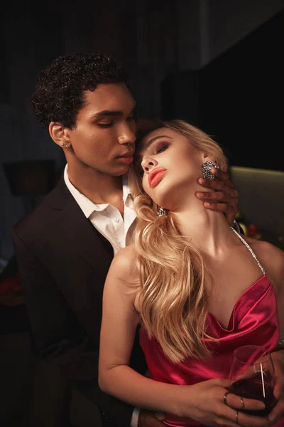Séduisant couple multiculturel sensuel en tenue de soirée avec accessoires étreignant amoureusement — Photo de stock
