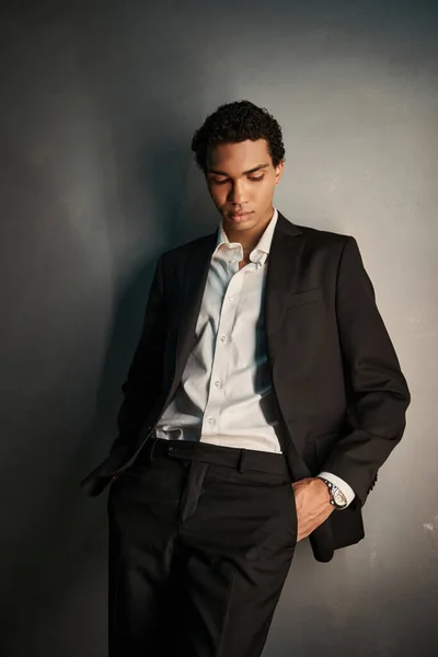 Handsome young african american man with piercing in black suit posing with hands in pockets — Stock Photo