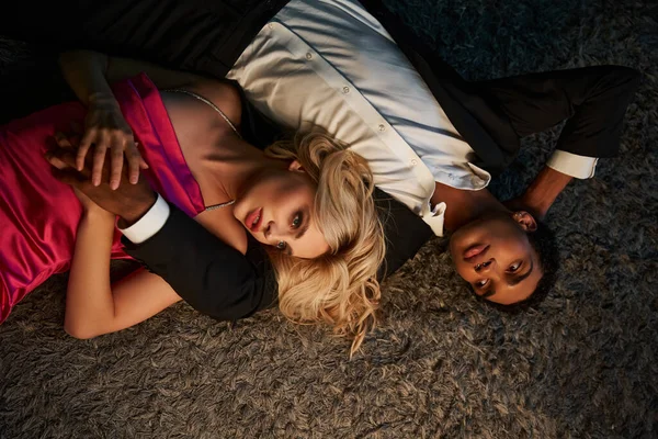 Привлекательная чувственная мультикультурная пара в вечерней одежде, позирующая и лежащая на диване вместе — стоковое фото