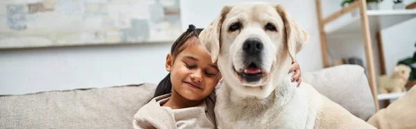 Happy girl sitting on couch with cute labrador in modern living room, animal companion banner — Stock Photo