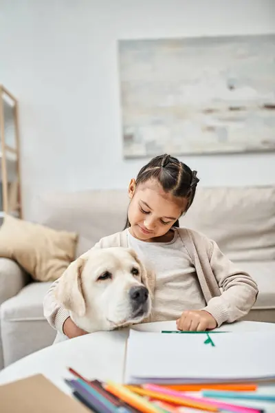 Little girl in casual clothes drawing and hugging labrador in modern living room, art and leisure — Stock Photo