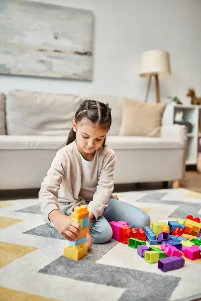 Elementary age girl playing with colorful toy blocks on carpet in living room, building tower game — Stock Photo