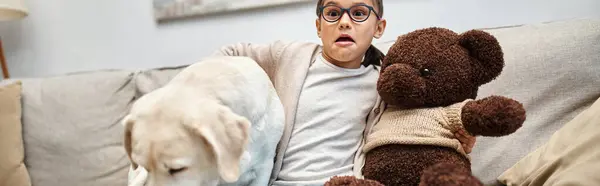 Scared girl in eyeglasses holding teddy bear and sitting with labrador while watching movie, banner — Stock Photo