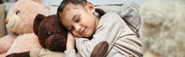 Adorable elementary age girl sleeping among soft teddy bears on couch in modern living room, banner — Stock Photo