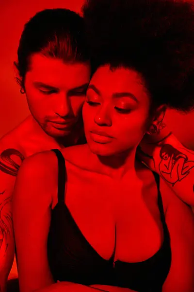 Bel homme avec des tatouages posant avec sa petite amie afro-américaine en soutien-gorge noir, couple sexy — Photo de stock