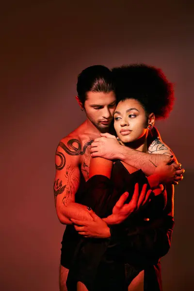 Hombre tatuado de buen aspecto abrazando amorosamente a su novia afroamericana por detrás, pareja sexy - foto de stock