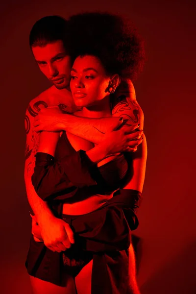 Hombre guapo abrazando amorosamente a su hermosa novia afroamericana por detrás, sexy pareja - foto de stock