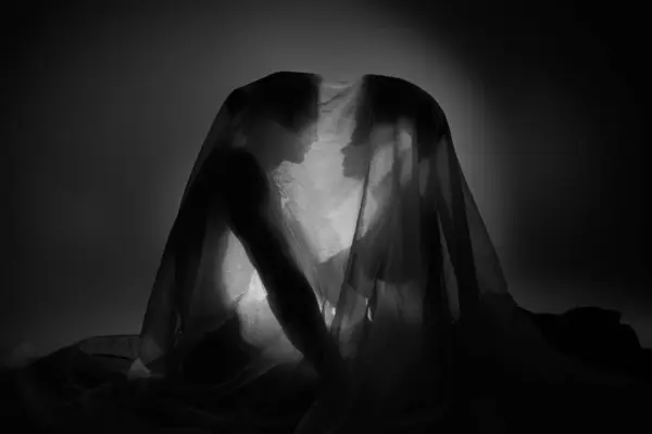 Black and white photo of sensual multiracial couple covered with bedsheet sitting on floor together — Stock Photo
