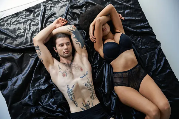 Appealing african american woman in lingerie lying in bed near her tattooed boyfriend, sexy couple — Stock Photo