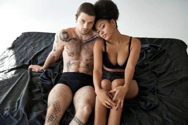 Diverse beautiful sexy couple in underwear sitting close to each other on bed, togetherness — Stock Photo