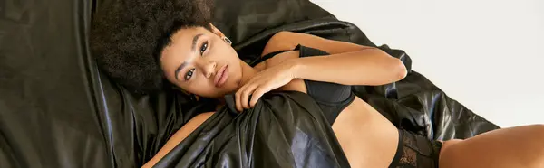 Привлекательная молодая африканская американка в нижнем белье лежит в постели и покрывает себя простыней — стоковое фото