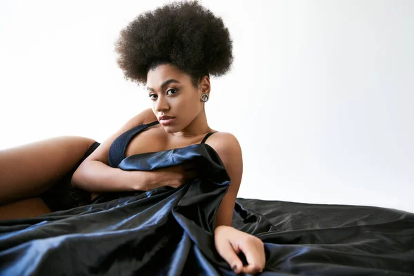 Draufsicht der schönen afrikanisch-amerikanischen Frau in Dessous auf dem Bett liegend und in die Kamera schauend — Stockfoto