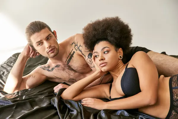 Young multicultural attractive couple in underwear lying in their bed together and looking away — Stock Photo