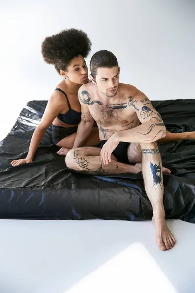 Gut aussehender Mann mit Tätowierungen sitzt auf dem Bett neben seiner afrikanisch-amerikanischen Freundin, sexy Paar — Stockfoto