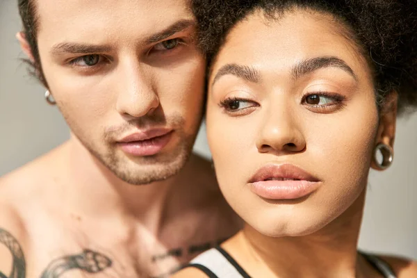 Handsome man with tattoos hugging warmly his pretty african american girlfriend on gray backdrop — Stock Photo