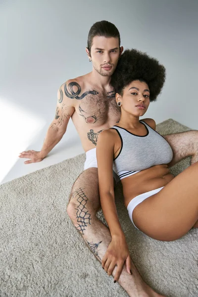 Alluring multicultural couple in comfy underwear sitting on floor and hugging each other warmly — Stock Photo