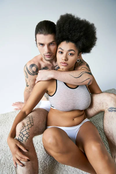 Alluring multiracial couple in comfy underwear sitting on floor and hugging each other lovingly — Stock Photo