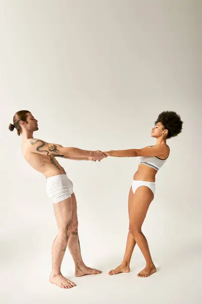 Beautiful multiracial sexy couple in underwear holding hands and looking at each other sensually — Stock Photo
