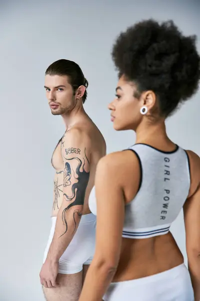 Focus on tattooed man with ponytail posing next to his blurred girlfriend and looking at camera — Stock Photo