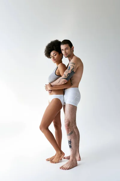 Tattooed man hugging warmly his beautiful african american girlfriend from behind, sexy couple — Stock Photo