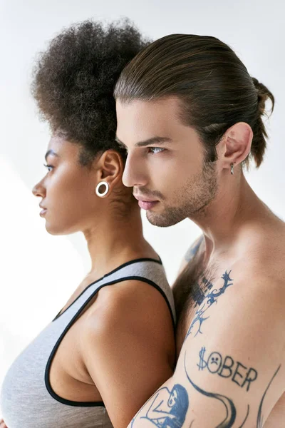 Guapo hombre tatuado abrazando a su hermosa novia afroamericana por detrás, sexy pareja - foto de stock