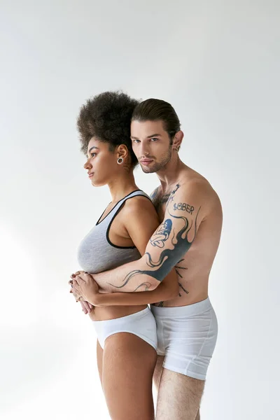 Appealing tattooed man hugging his beautiful african american girlfriend from behind, sexy couple — Stock Photo