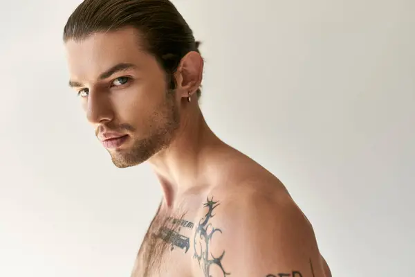 Verführerischer junger Mann mit Pferdeschwanz und coolen Tattoos in bequemer Unterwäsche posiert auf Ecru-Hintergrund — Stockfoto