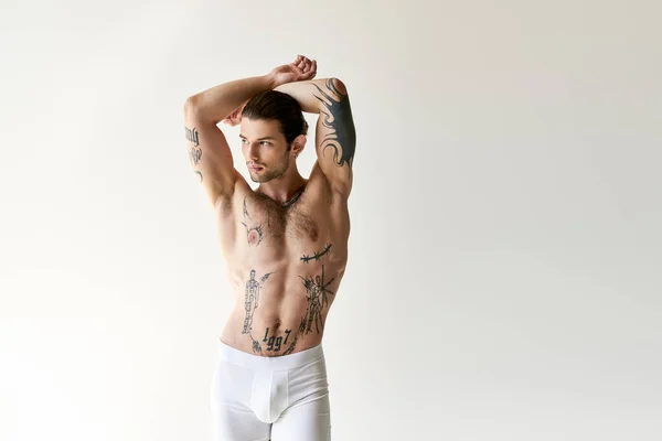 Sexy verführerischer Mann mit Pferdeschwanz und coolen Tattoos in bequemer Unterwäsche posiert auf ecru Hintergrund — Stockfoto