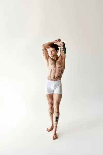 Sexy attractive man with ponytail and cool tattoos in comfy underwear posing on ecru background — стоковое фото