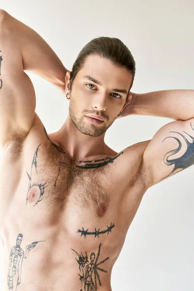 Sexy guapo hombre con cola de caballo y fresco tatuajes en ropa interior cómoda posando sobre fondo crudo - foto de stock