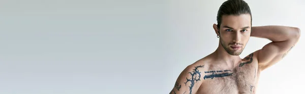 Good looking man with ponytail and tattoos in comfy underwear posing on ecru background, banner — Stock Photo