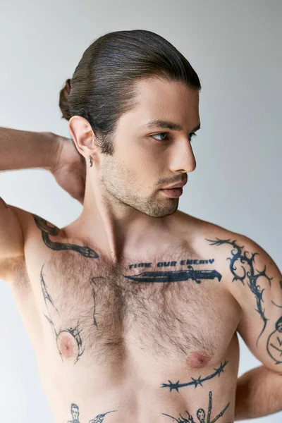 Sexy hombre guapo con cola de caballo y tatuajes en ropa interior cómoda posando sobre fondo crudo - foto de stock