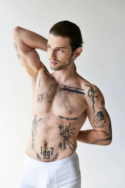 Молодой симпатичный мужчина с хвостиком и татуировками в удобном нижнем белье позирует на фоне экру — стоковое фото