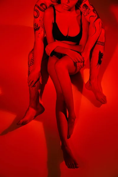 Обрізаний чоловік з татуюваннями позує зі своєю афроамериканською подругою в чорному бюстгальтері, сексуальна пара — стокове фото
