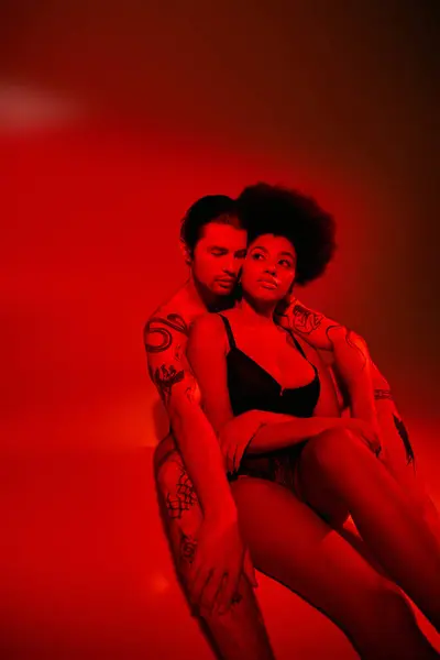 Hombre guapo con tatuajes con su novia afroamericana bonita en luces, pareja sexy - foto de stock