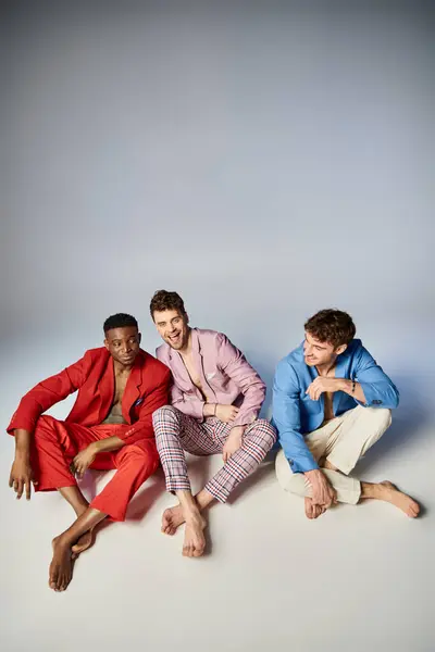 Fröhliche Männer in hellen Anzügen, die mit überkreuzten Beinen auf dem Boden sitzen und fröhlich lächeln — Stockfoto