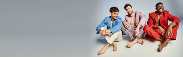 Allegri uomini diversi in abiti luminosi seduti sul pavimento con le gambe incrociate e sorridenti gioiosamente, banner — Foto stock