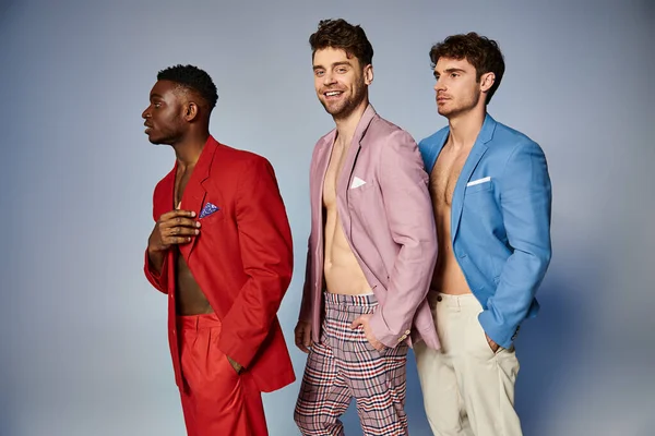 Cheerful appealing diverse men in stylish vibrant suits posing in single file on gray backdrop — Stock Photo