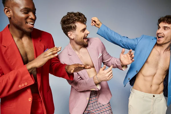 Cheerful multicultural friends in vibrant elegant suits posing together on gray backdrop, fashion — Stock Photo