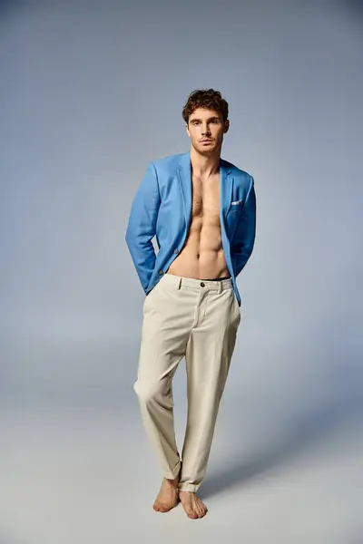 Молодой привлекательный мужчина в яркой расстегнутой синей куртке позирует на сером фоне, концепция моды — стоковое фото
