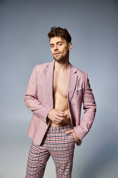 Bel homme en costume rose vif déboutonné posant allègrement sur fond gris, concept de mode — Photo de stock