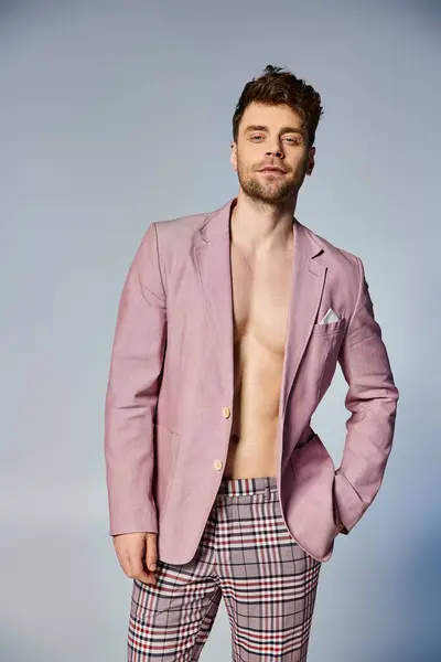 Красивий стильний чоловік у яскраво-рожевому костюмі, який привабливо позує на сірому тлі, мода — стокове фото