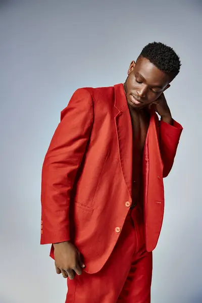 Привлекательный африканский американец в ярком красном одеянии позирует на сером фоне, концепция моды — стоковое фото